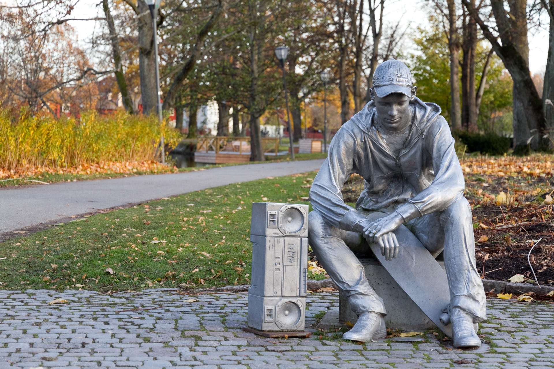 Silverfärgad man med keps sitter på marken med sin skateboard framför sig.