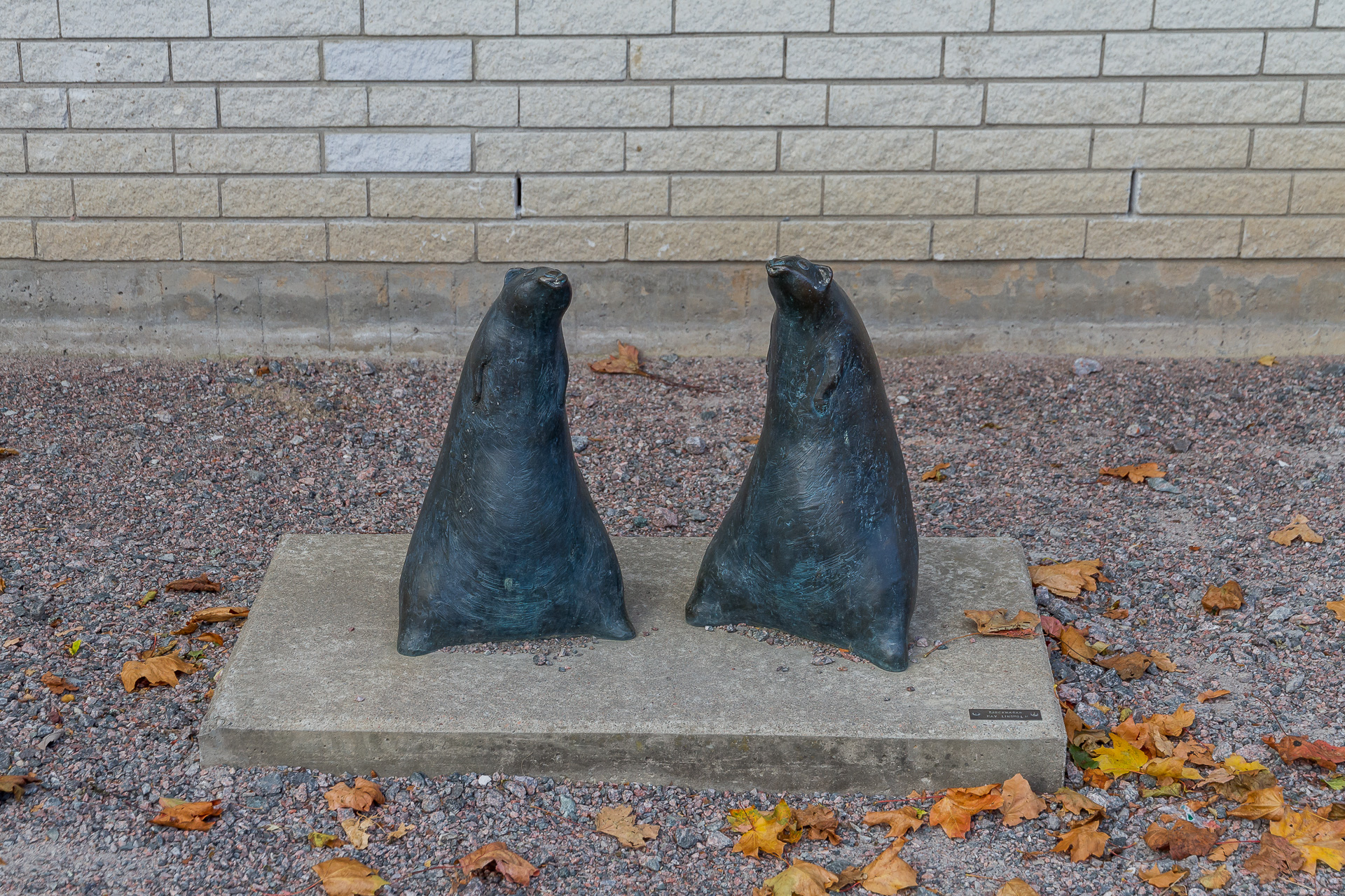 Två sälliknande figurer i mörkgrå brons står på sina knappt synliga bakben och blottar sina runda magar. 