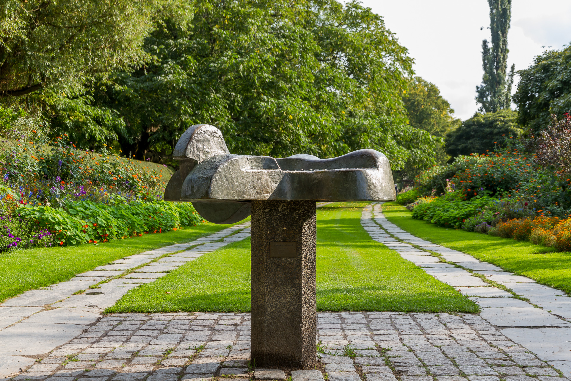 På en smal, rektangulär stensockel ligger en urgröpt formation i brons. Den kan liknas vid en liggande fågel.